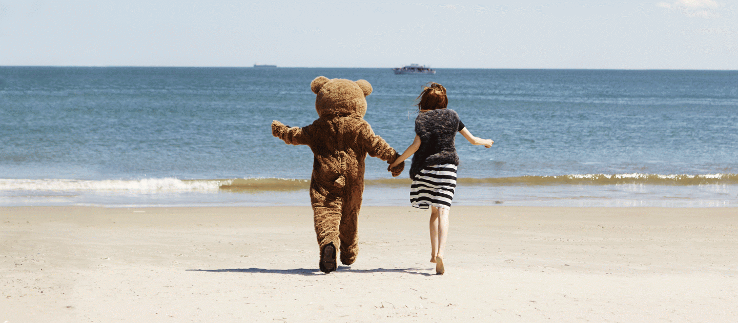 Ein Teddy und eine Frau spazieren am Strand