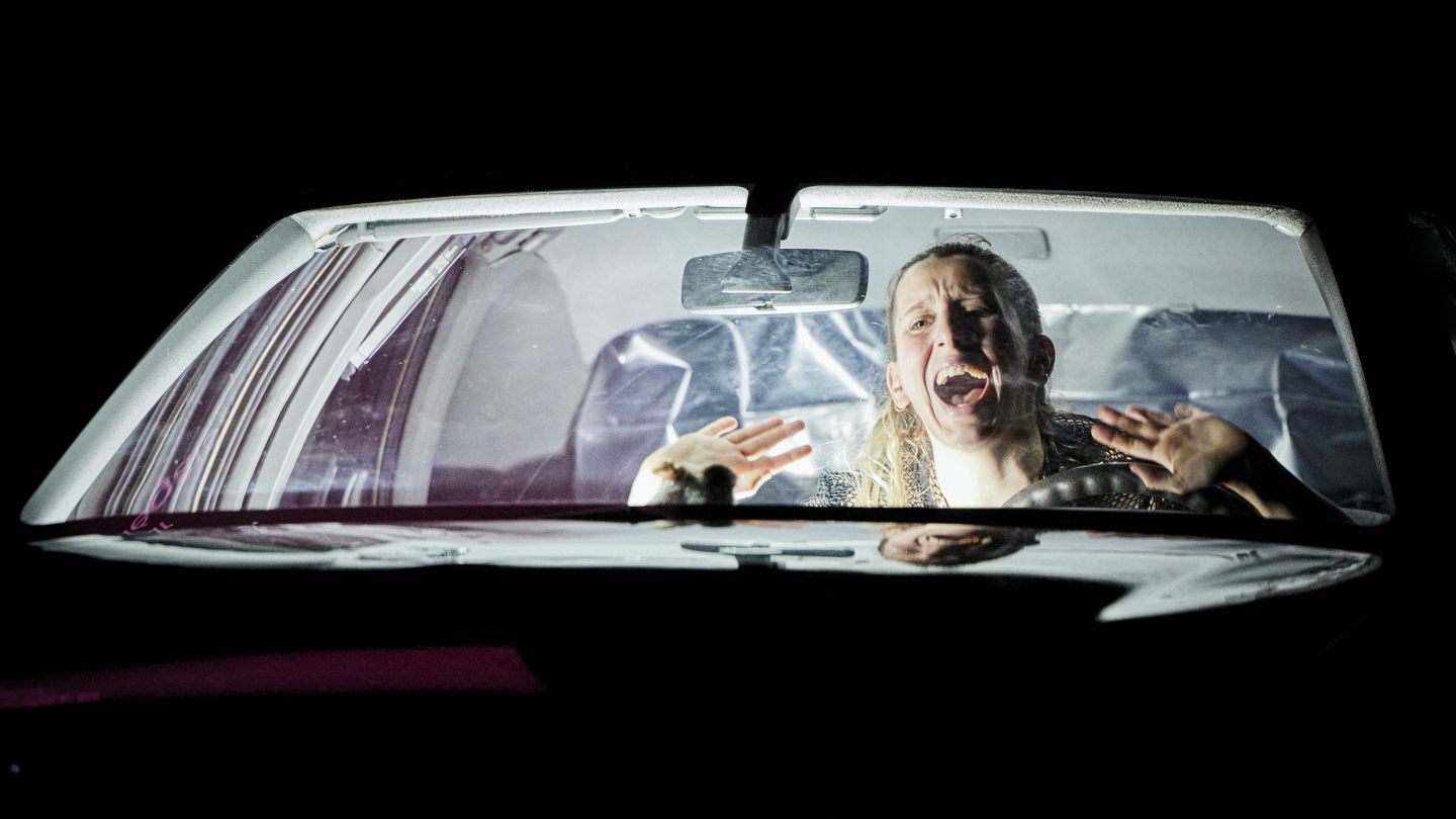 Ein*e Performer*in schreiend im Auto während der Vorstellung "The CADELA FORÇA TRILOGY"