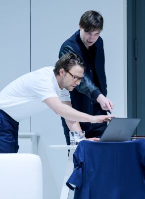 Alexandros Koutsoulis und Janek Maudrich in ihren Rollen, die auf einen Laptop schuaen und zeigen.