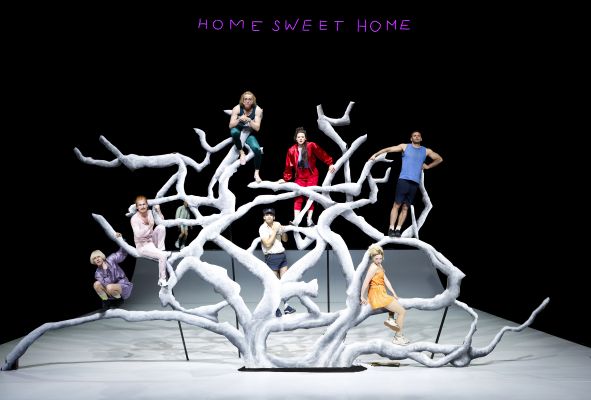 Das Ensemble steht auf der Bühne auf einem weißen Baum und blickt in den Zuschauerraum.