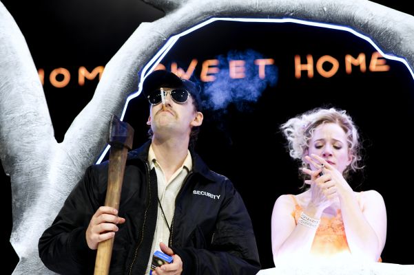 Alexandros Koutsoulis, Henriette Nagel in ihren Rollen stehen nebeneinander auf der Bühne und rauchen. Er trägt eine Securityjacke und hält eine Axt auf der Schulter.