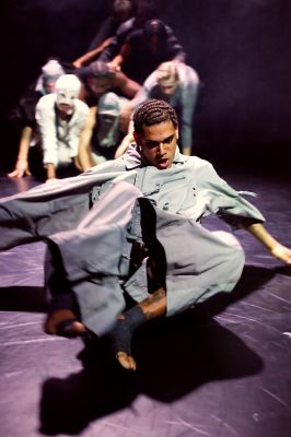 Eine Person breakt auf dem Boden vor eine Gruppe weiterer Tänzer*innen.