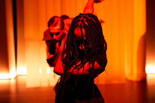 Zwei Personen vor einem orange beleuchtetem Vorhang tanzen gebückt.