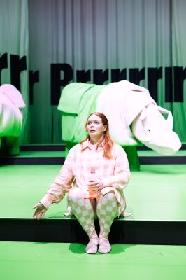 Eine Person sitzt auf einer Stufe. Hinter ihr stehen zwei pink-grüne Nashörner.