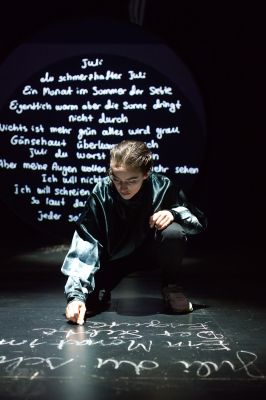 Ruth Bohsung schreibt mit Kreide das Gedicht &quot;Juli&quot; auf den Boden. Im Hintergrund ist es auf eine Wand projiziert.
