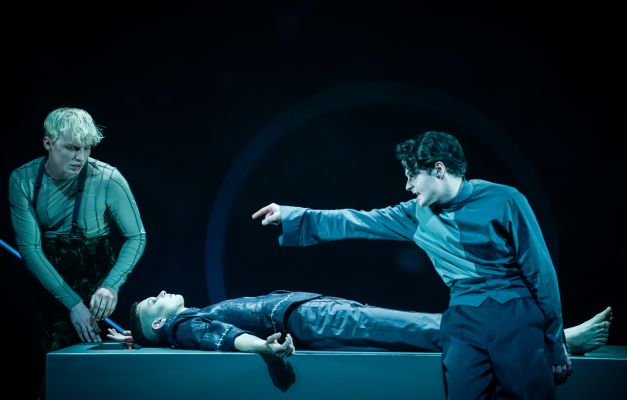 Frankenstein_Anton Nürnberg, Nina Noé Stehlin, Cedric Stern (c) Arno Declair Anton Nürnberg sitzt, Nina Noé Stehlin liegt, Cedric Stern zeigt auf Anton Nürnberg.