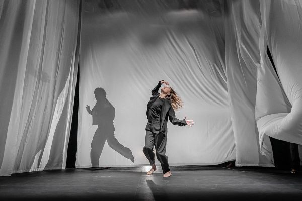 Eine Frau tanzt auf der Bühne und ihr Schatten wird an die Leinwand projiziert.