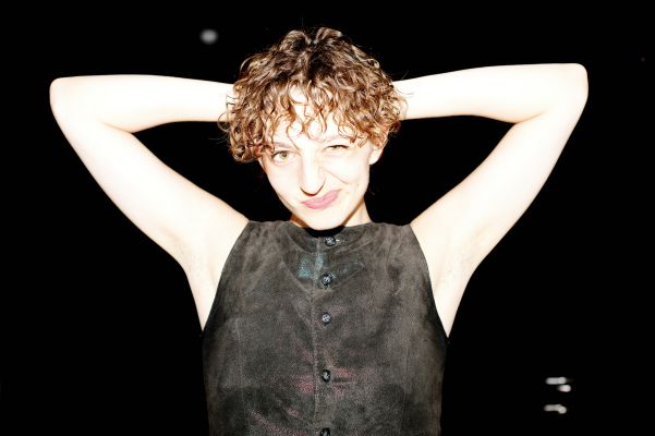 Marlene Markt hält ihre Arme verschränkt hinter ihrem Kopf und zwinkert verschmitzt in die Kamera