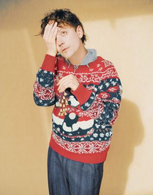 Oehl (c) Tim Cadavini Ariel Oehl trägt einen Weihnachtspullover. Er hält eine Hand vor ein Auge, in der anderen hat er kleine Glöckchen.