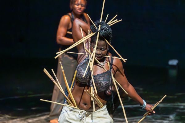 Eine Performerin steckt sich dünne Holzstäbe durch Haare und Kleidung.