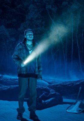 Jawad Rajpoot steht mit einer Taschenlampe in der Sumpflandschaft des Bühnenbilds. Sein Blick folgt verängstigt dem Schein der Taschenlampe.