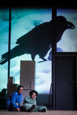 Ruth Bohsung und Cedric Stern lungern auf dem Boden. Im Hintergrund ist eine große projizierte Krähe zu sehen.