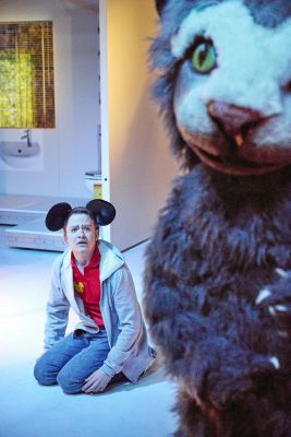 Niklas Hummel kniet auf dem Boden. Er trägt Mickey Mouse Ohren. In seinem Blick liegt Verzweiflung. Im Bildvordergrund steht ein als Katze verkleideter Darsteller, der jedoch nicht ganz im Bild ist.