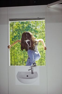 Luise Hart klettert durch ein Fenster. Ihr Gesicht wird verdeckt von einer Ghostface Maske. Unter dem Fenster klebt ein Bild eines Waschbeckens und hinter ihr sind Bäume erkennbar.