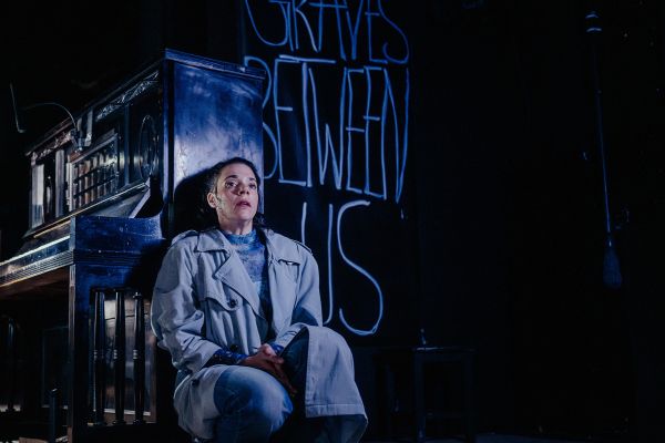 Eine Darstellerin sitzt, den Rücken an die Seitenwand eines Klavieres gelehnt, in der Hocke.