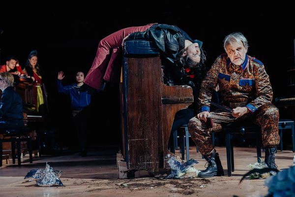 Bild vom Ensemble. Eine Darstellerin liegt auf einem Klavier. Ein anderer sitzt auf einem Klavierhocker.