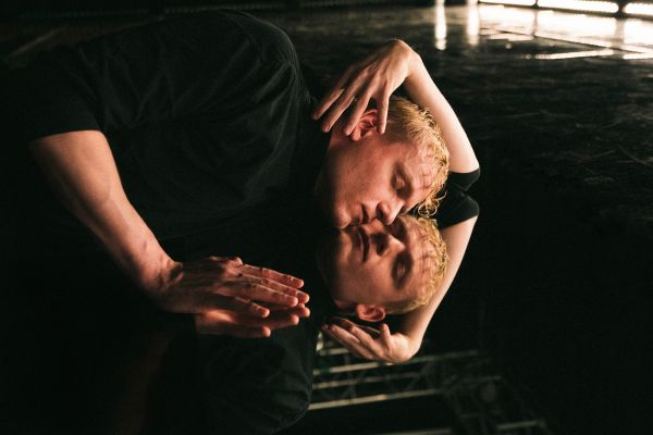 Johannes Hegemann liegt in schwarzem Rollkragenpullover mit geschlossenen Augen auf dem Boden, welcher ihn spiegelt