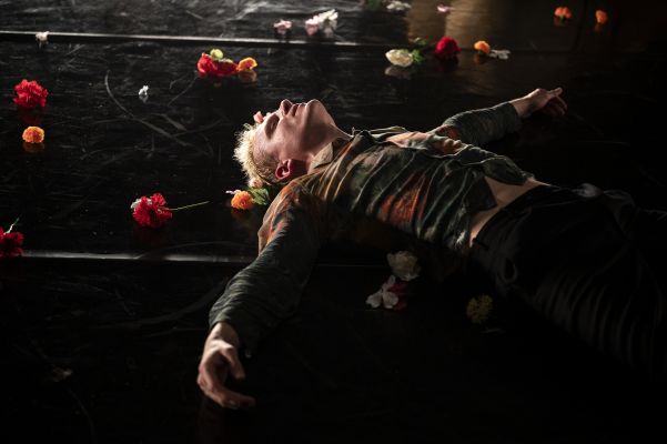 Johannes Hegemann liegt mit ausgebreiteten Armen auf dem Boden. Um ihn herum verteilt sind Blumen. Sein Blick richtet sich gen Decke.