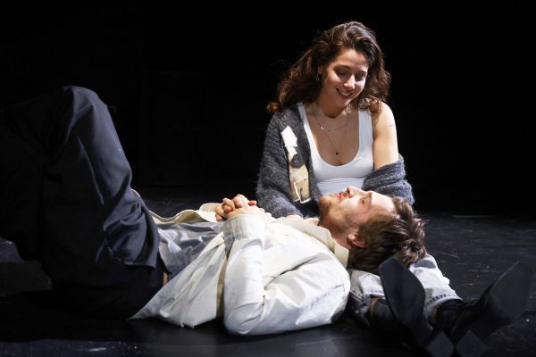 Ein Mann liegt mit dem Kopf auf den Beinen einer Frau. Sie blickt lächelnd auf ihn herab.