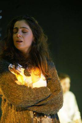 Eine Schauspielerin mit langen braunen Haaren spricht mit geschlossenen Augen und verschränkten Armen.