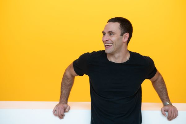 Portraitfoto von einem lachenden Jonathan Müller vor einer gelben Wand