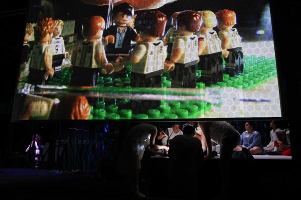 Über dem Ensemble werden Lego-Fußballspieler auf die Wand projiziert.
