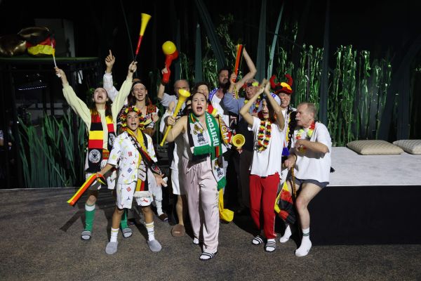 Menschen verschiedenen Alters, die unterschiedliche Fanartikel tragen, stehen in einem Pulk und jubeln.