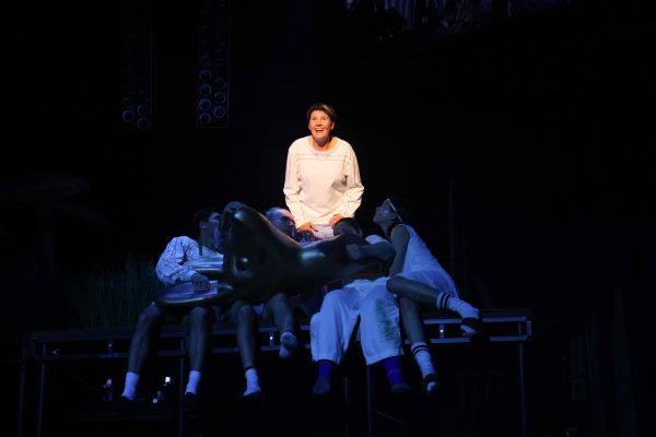 Lisa Guth mit freudigem Blick. Vier Ensemblemitglieder sitzen eng um sie. Quer über ihnen liegt ein menschengroßer Rehkopf.