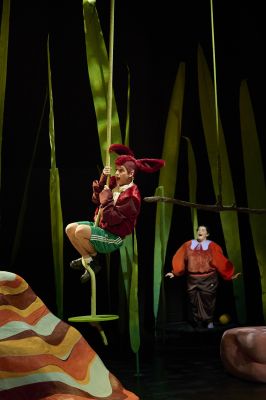 Ein Schauspieler schwingt an einem Seil, eine zweite Schauspielerin steht mit aufgerissenem Mund im Hintergrund.
