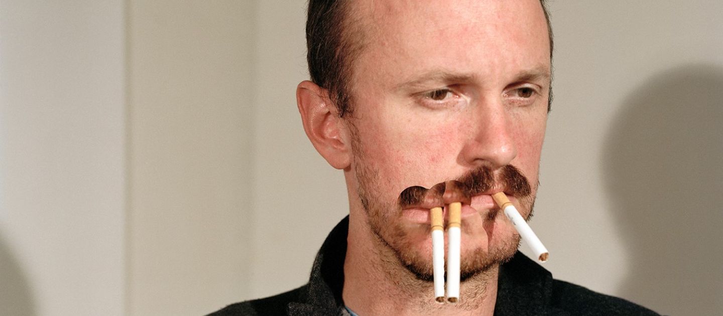 Das Foto zeigt einen traurigen Mann, der 3 Zigaretten im Mund hat.
