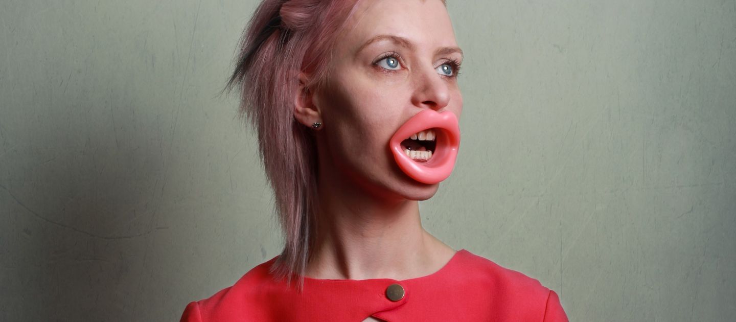 Plakatmotiv von Unser Fleisch, unser Blut. Auf dem Bild ist eine Frau in rosa, mit übernatürlich großem Mund zu sehen.