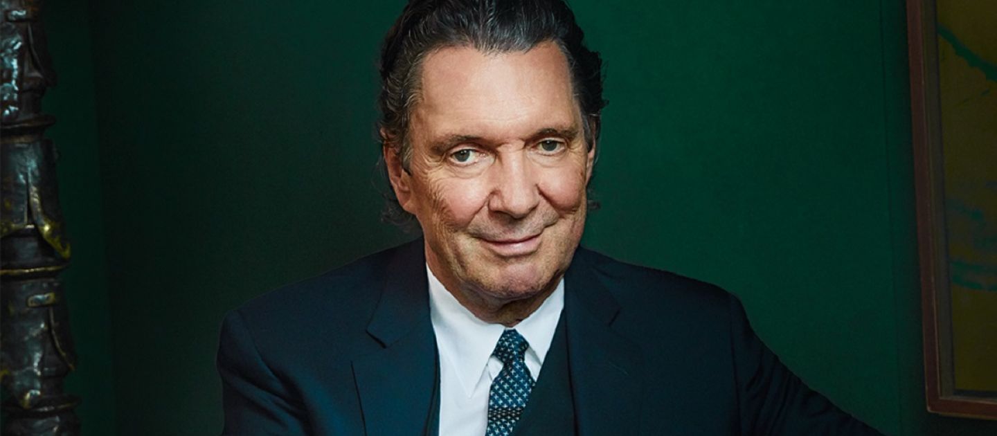 Das Bild zeigt eine Portraitaufnahme von Martin Suter in Anzug und vor einem dunkelgrünen Hintergrund.