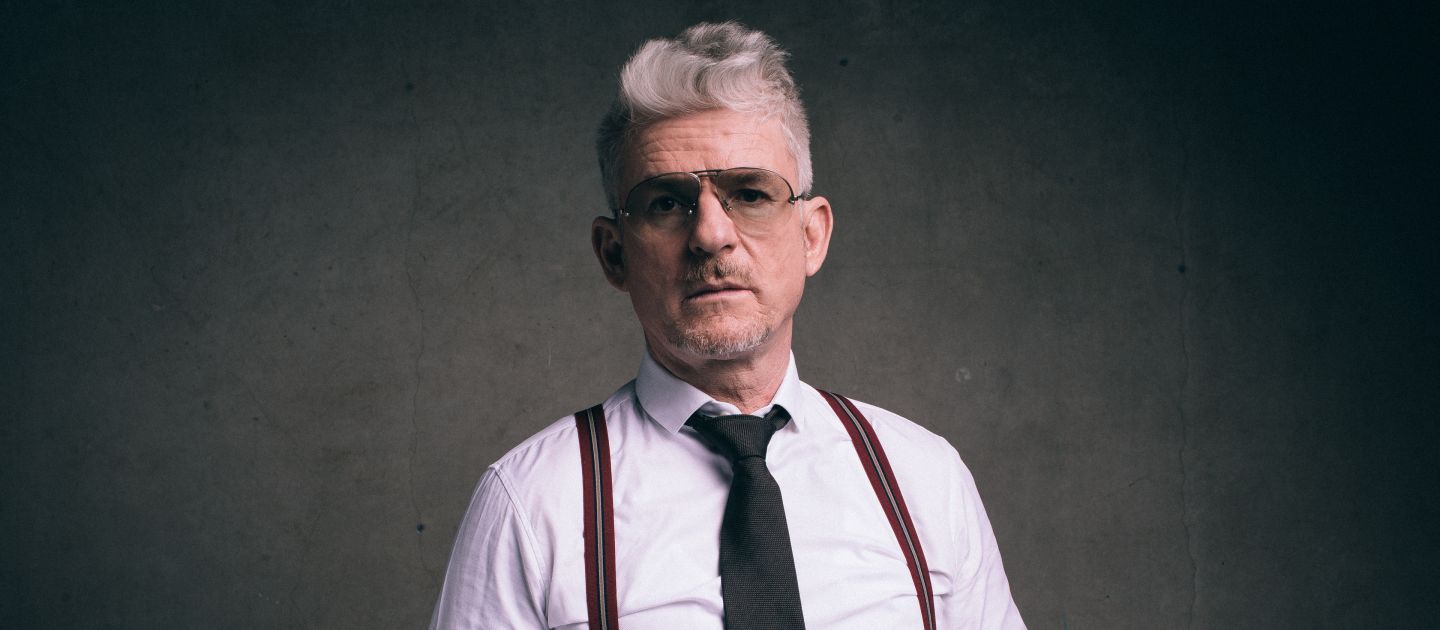 Heinz Strunk © Dennis Dirksen Ein Portraitfoto von Dennis Dirksen stehend von einer grauen Wand