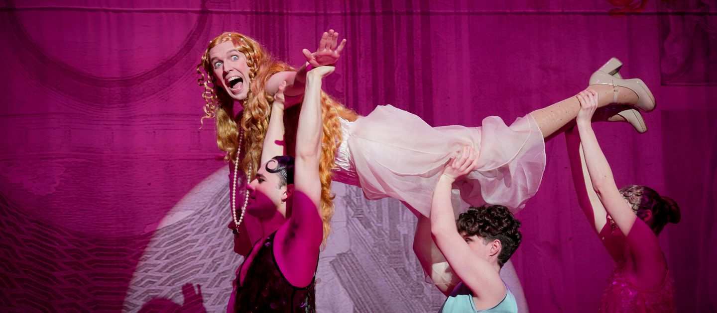 Caligula im Venuskostüm wird von drei anderen gehoben und "fliegt".