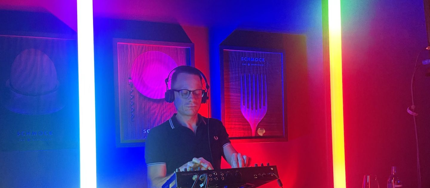 DJ Modeptobias am DJ Pult, neben ihm erleuchten 2 bunte Neonröhren das Pult