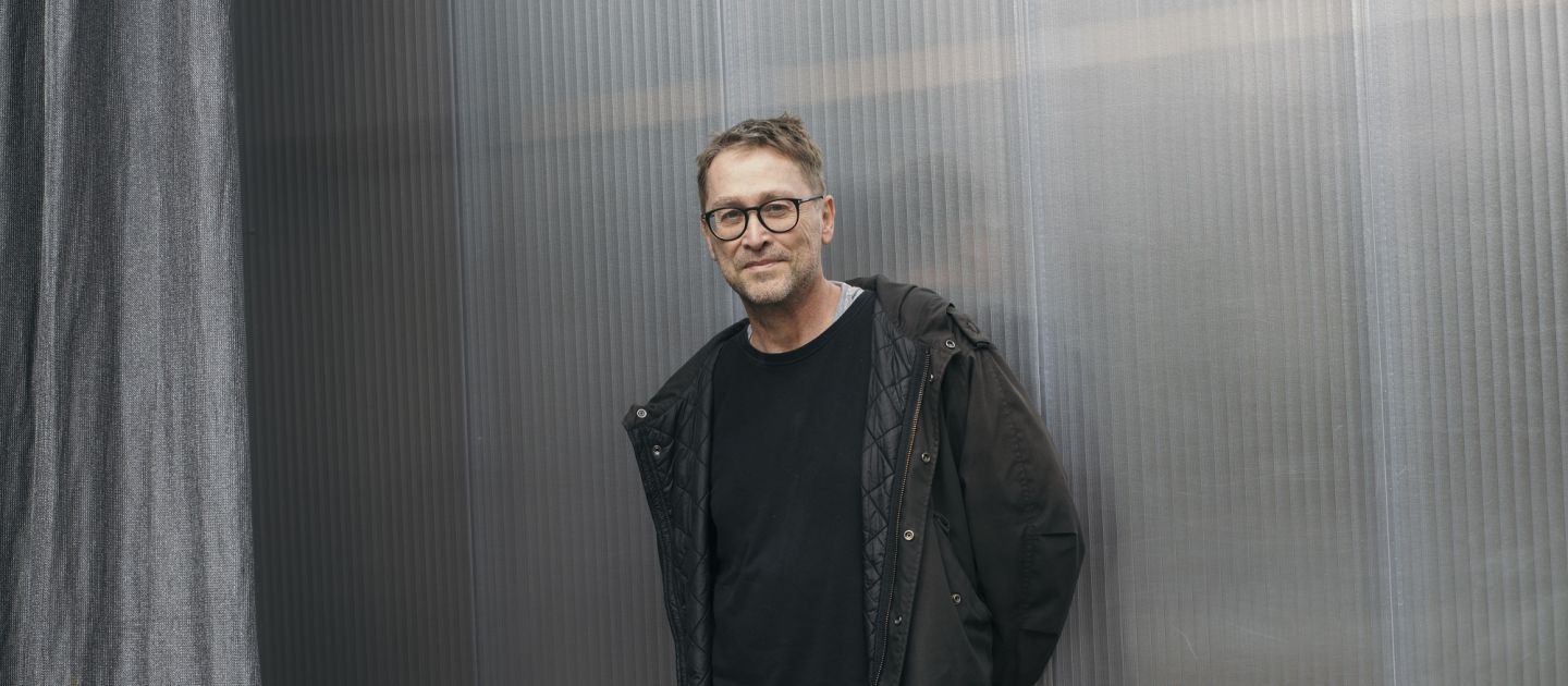 Jan Weiler lehnt an einer Wand mit verschränkten Armen hinter dem Rücken.