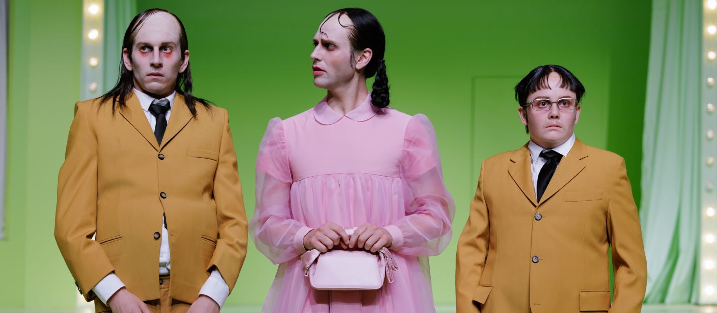 The Lobster (c) Marcella Ruiz Cruz Zwei Schauspieler*innen in senfgelben Anzügen, zwischen ihnen ein*e Schauspieler*in in rosa Tüllkleid
