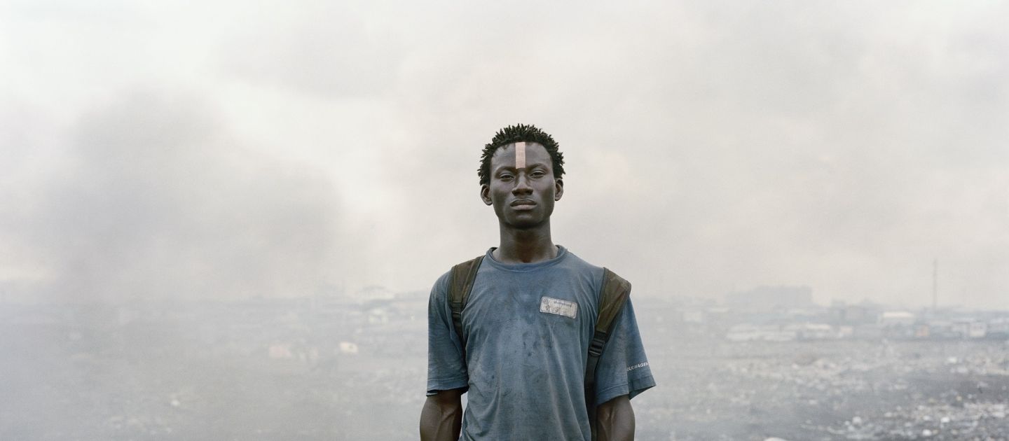 Ein junger Schwarzer Mann steht mit einer Hacke in der Hand inmitten von Schutt und Rauchwolken