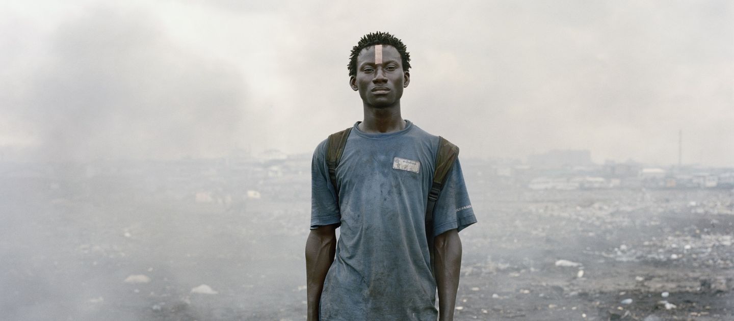 Ein junger Schwarzer Mann steht mit einer Hacke in der Hand inmitten von Schutt und Rauchwolken