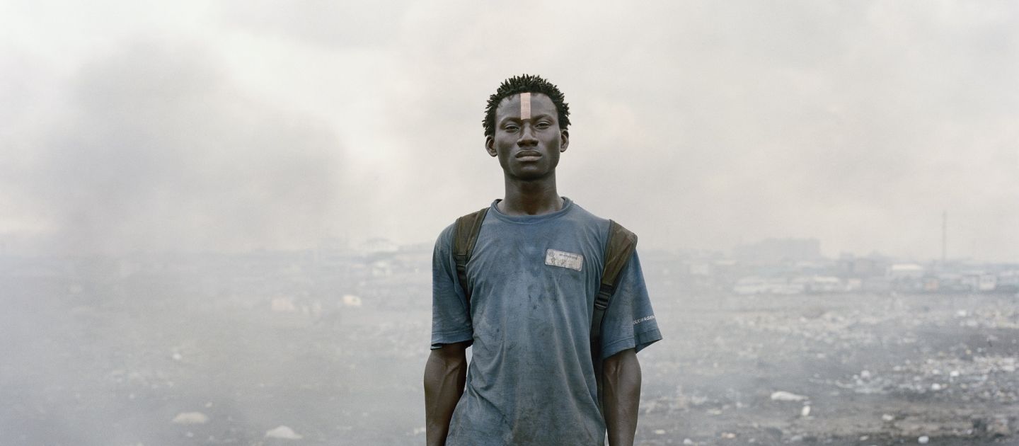 Ein junger Schwarzer Mann steht mit einer Hacke in der Hand inmitten von Schutt und Rauchwolken