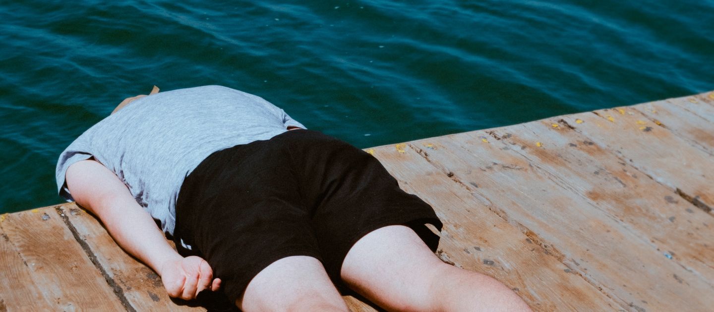 Das Plakatmotiv zeigt zeigt eine Person, die mit dem Bauch auf einem Steg liegt. Von den Schultern ab hängt der Körper über den Rand des Stegs hinaus, der Kopf ist nicht zu sehen.