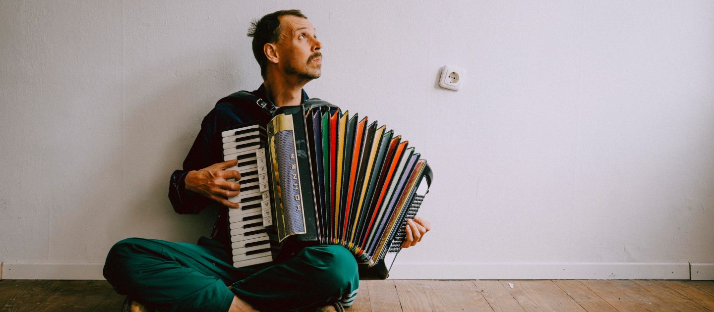 Maxi Pongratz sitzend mit Akkordeon vor einer weißen Wand, sein Kopf ist in Richtung der rechten oberen Ecke des Bild gedreht.t.