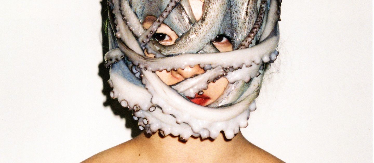 Eine Person vor weißem Hintergrund. Um ihren Kopf ist ein Oktopus gewickelt.