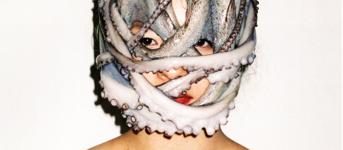 Eine Person vor weißem Hintergrund. Um ihren Kopf ist ein Oktopus gewickelt.
