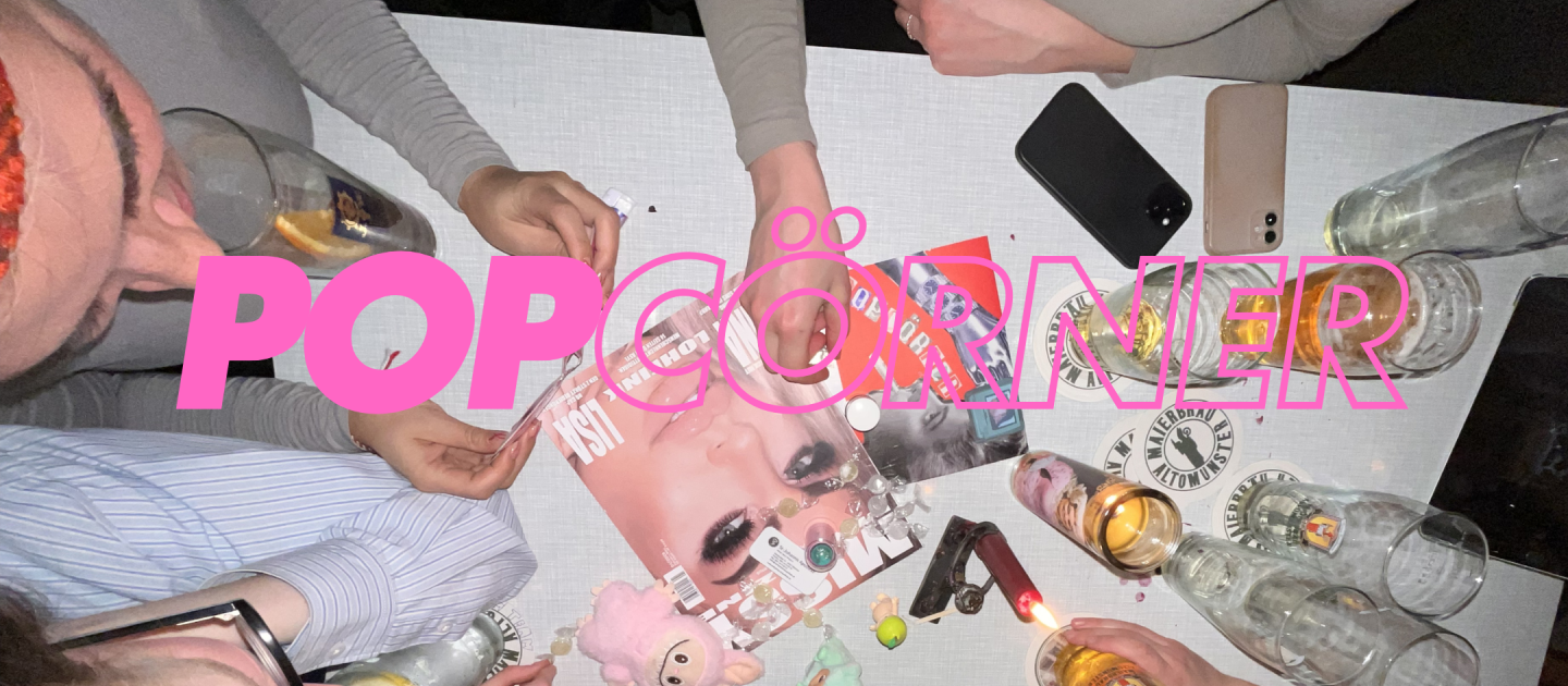 Ein Foto von einem Tisch voller Magazine und Gläser. Ringsherum sitzt eine Gruppe Frauen.