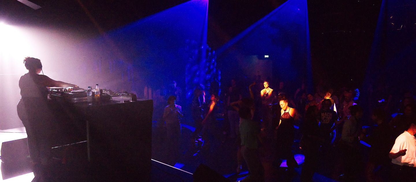 Ein Partyfoto vom Radikal jung 2025: links ist DJ Alba am Mischpult, rechts tanzt die Menge.