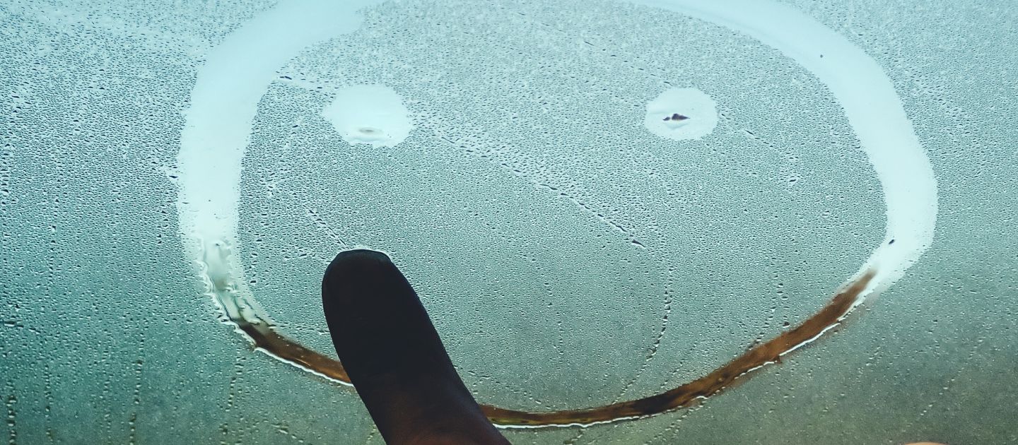 Eine Hand malt einen Smiley auf ein beschlagenes Glas.