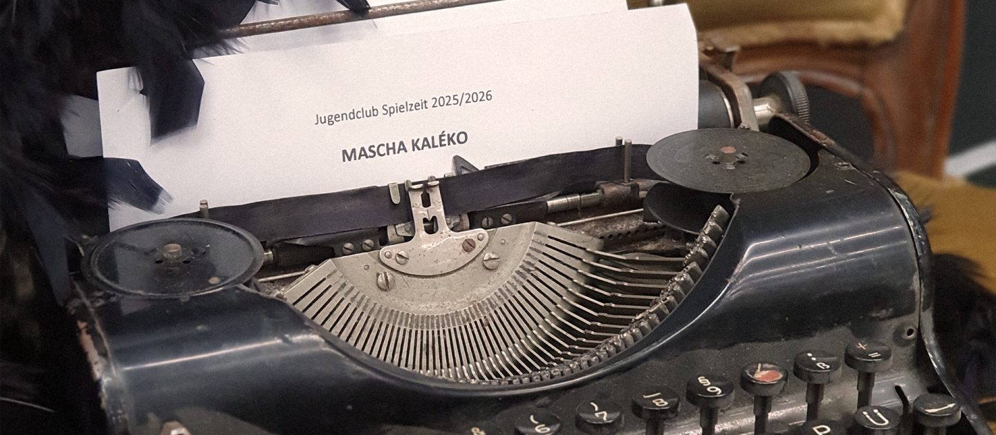 Eine Schreibmaschine aus der ein Blatt ragt. Darüber ist eine schwarze Federboa drapiert.