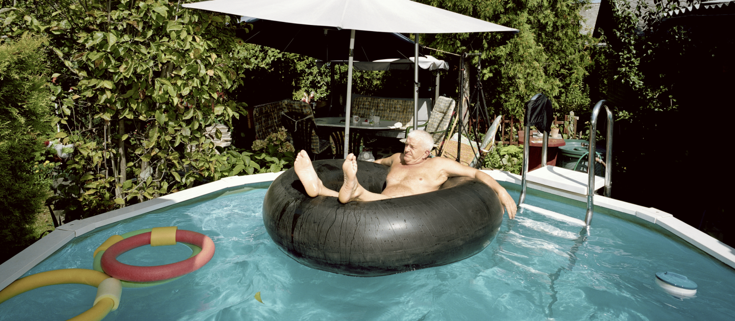 Ein alter Mann sitzt in einem Schwimmring in einem Gartenpool.