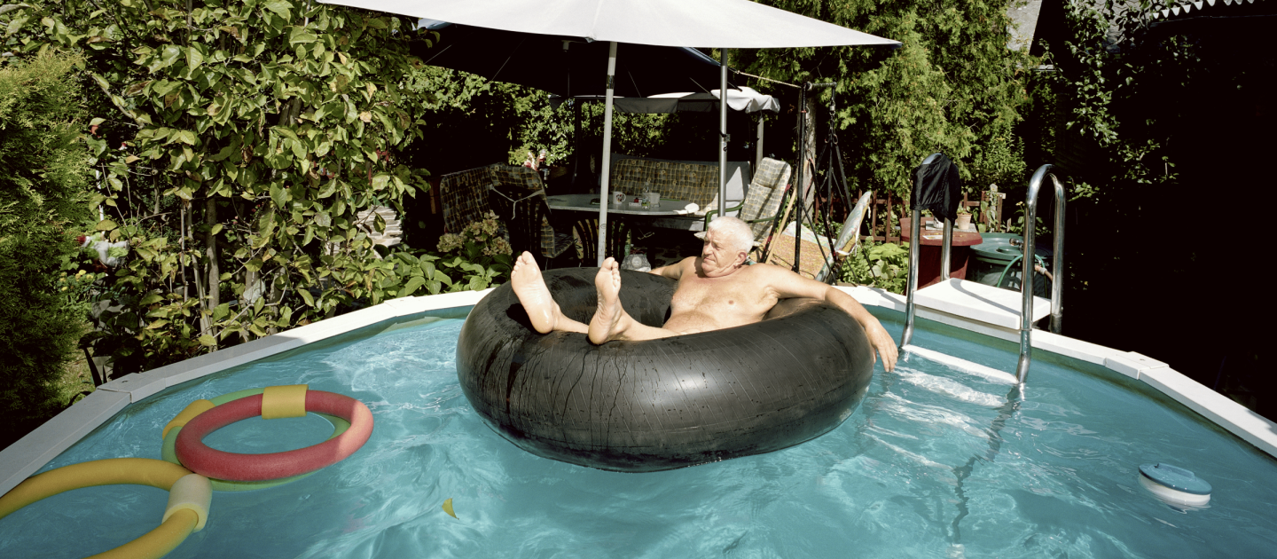 Ein alter Mann sitzt in einem Schwimmring in einem Gartenpool.